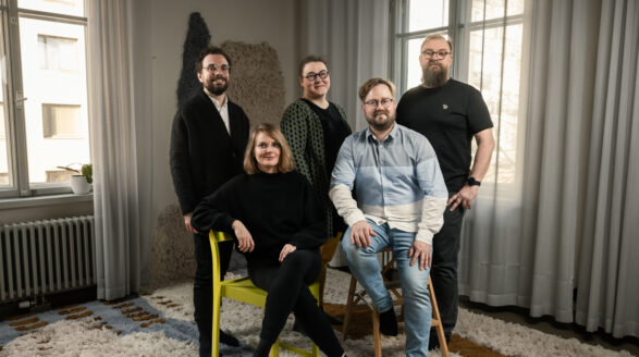 Viisi hymyilevää ihmistä huoneessa.