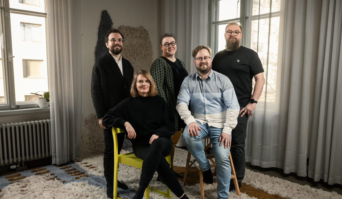 Viisi hymyilevää ihmistä huoneessa.